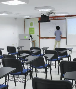 Classroom showing the desks and a teacher erasing the board.
