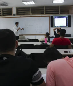 General shot showing the students in their chairs and the professor explaining on the board.