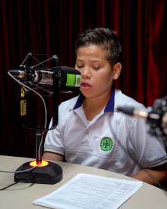 School student narrating a story into a recording booth microphone